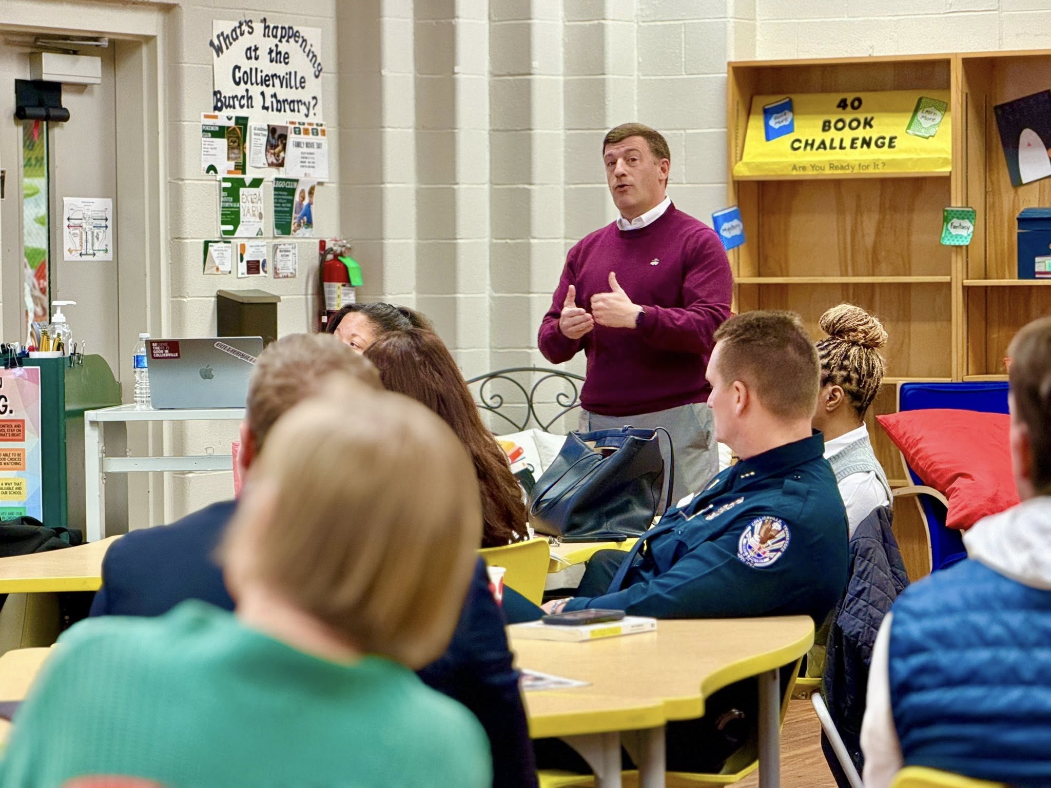 A person standing in a classroom setting talking to adults sitting at tables.